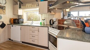 A compact kitchen with a microwave, sink, and stove. There is a window providing natural light, and the kitchen features wooden cabinets and a countertop. - 5 Star Holiday Home in Oster Assels (Øster Assels)