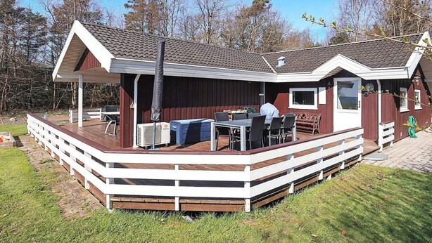 A covered outdoor area with a table and chairs, a barbecue grill, and a small building with a window. - 5 Star Holiday Home in Oster Assels (Øster Assels)