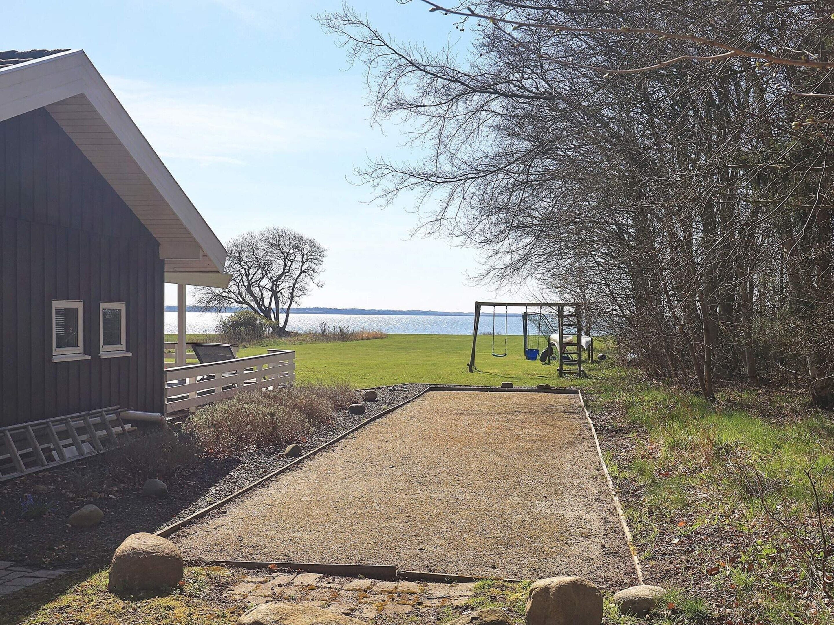 A house with a gravel path leading to a swing set, a fenced area, and a view of a lake.