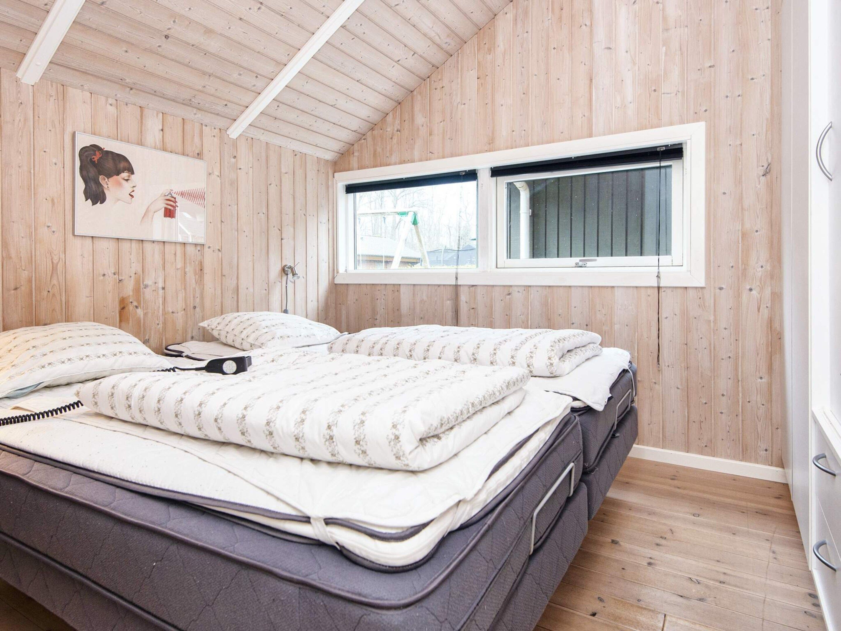 Un dormitorio con techo de madera, una ventana, una cama con colchón y almohadas, y un cuadro colgado en la pared.