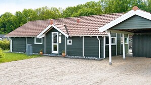 A single-story building with a sloped roof, a covered porch, and a gravel driveway. - 5 Star Holiday Home in Juelsminde (Horsens)
