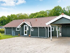 En enplansbyggnad med ett sluttande tak, en inglasad veranda och en grusuppfart.