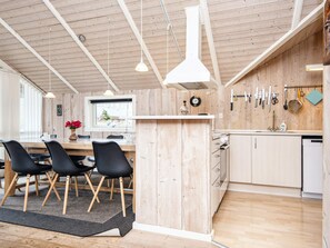 A modern kitchen with wooden accents, a dining area with black chairs, and a kitchen island. - 5 Star Holiday Home in Juelsminde (Horsens)