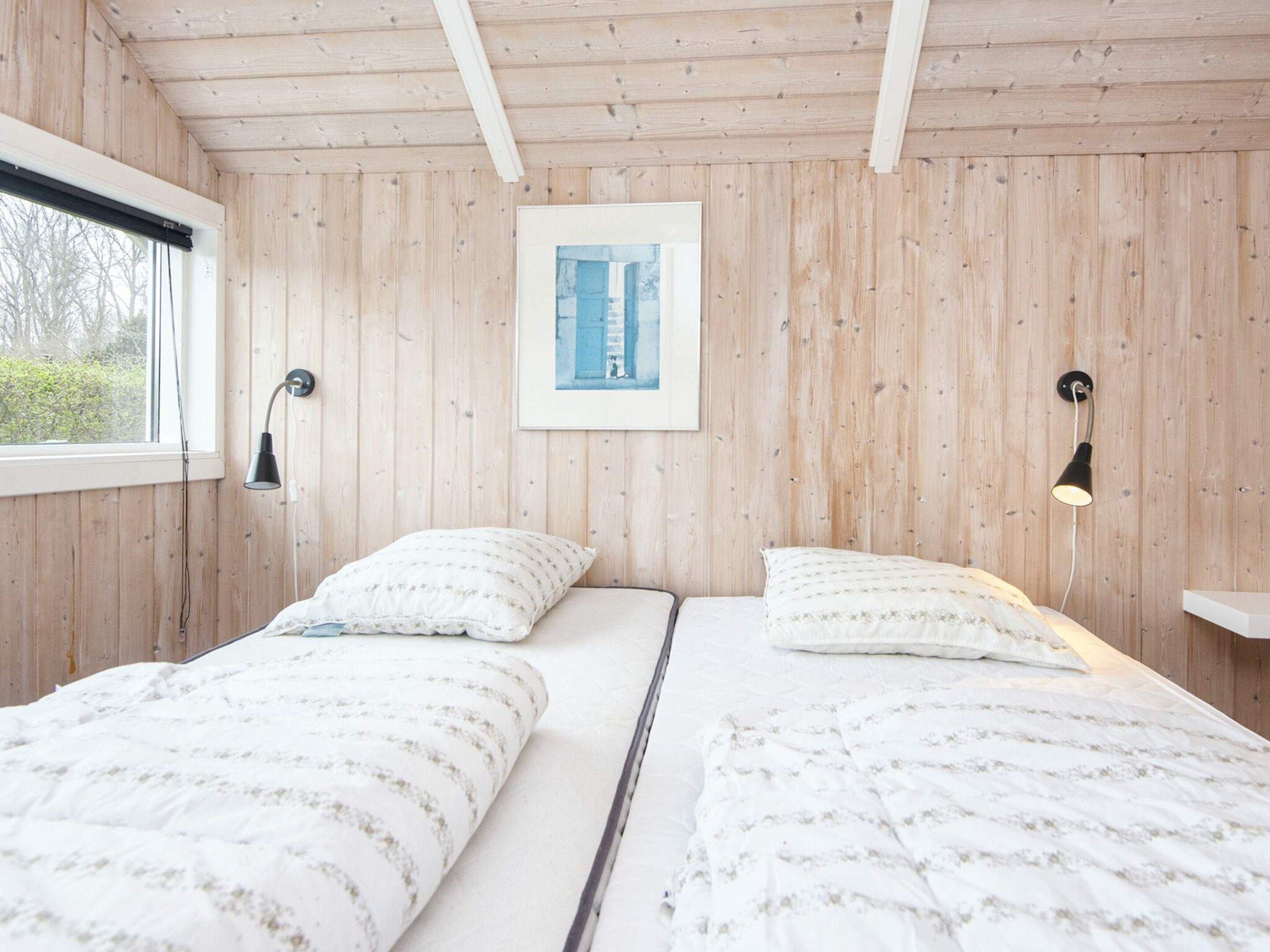 Ein Zimmer mit Holzwänden, einem Bett mit gemusterten Betttextilien, einem gerahmten Bild an der Wand und einem Fenster mit Blick auf Bäume.