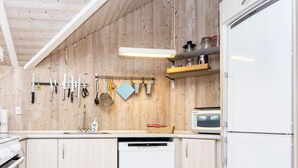 A kitchen with wooden walls, a dishwasher, a microwave, and various kitchen utensils hanging on the wall. - 5 Star Holiday Home in Juelsminde (Horsens)