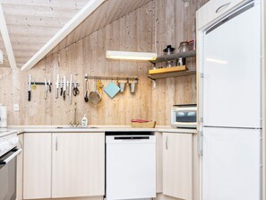 A kitchen with wooden walls, a dishwasher, a microwave, and various kitchen utensils hanging on the wall.