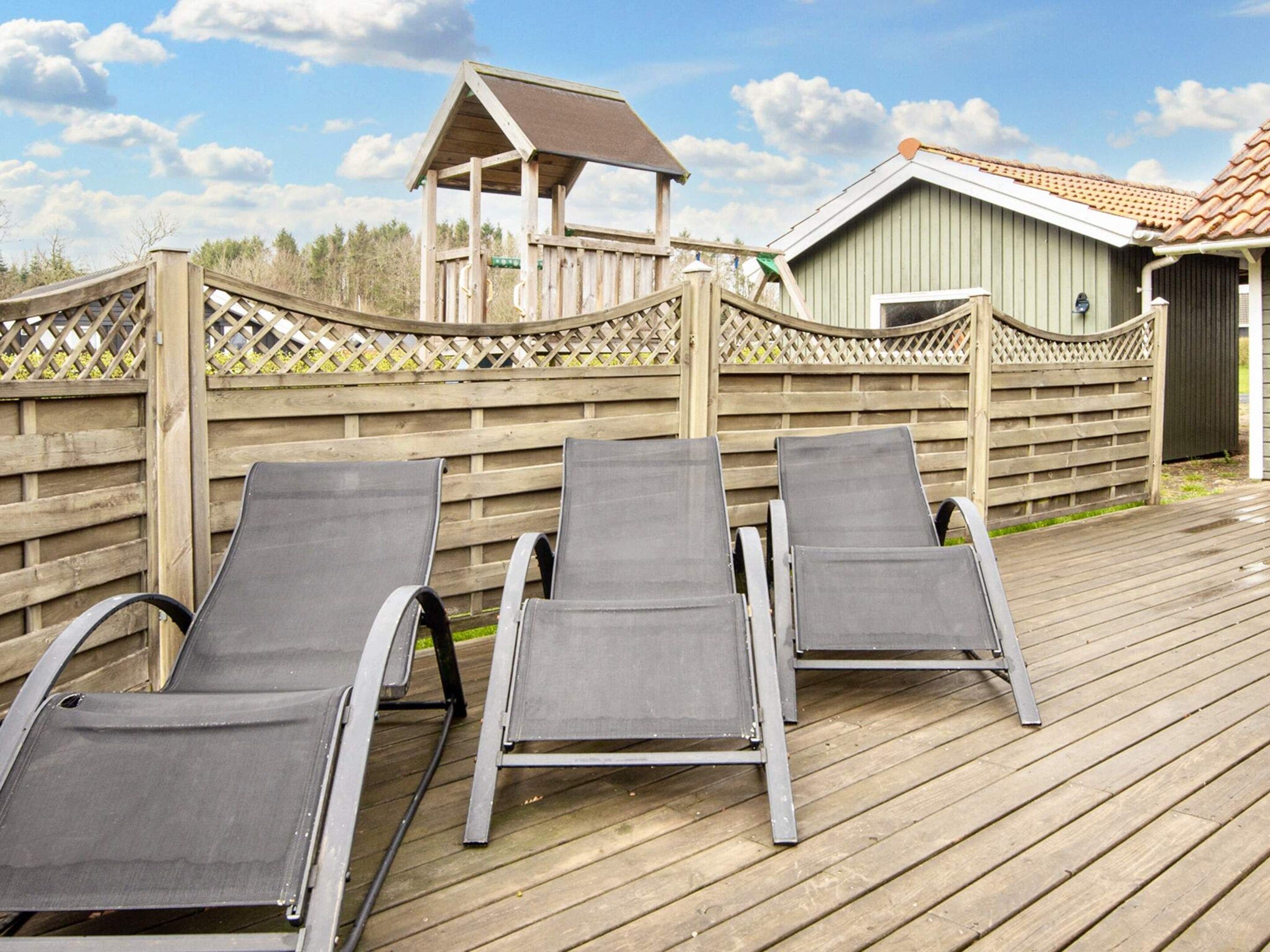 A wooden deck with three lounge chairs and a small gazebo.