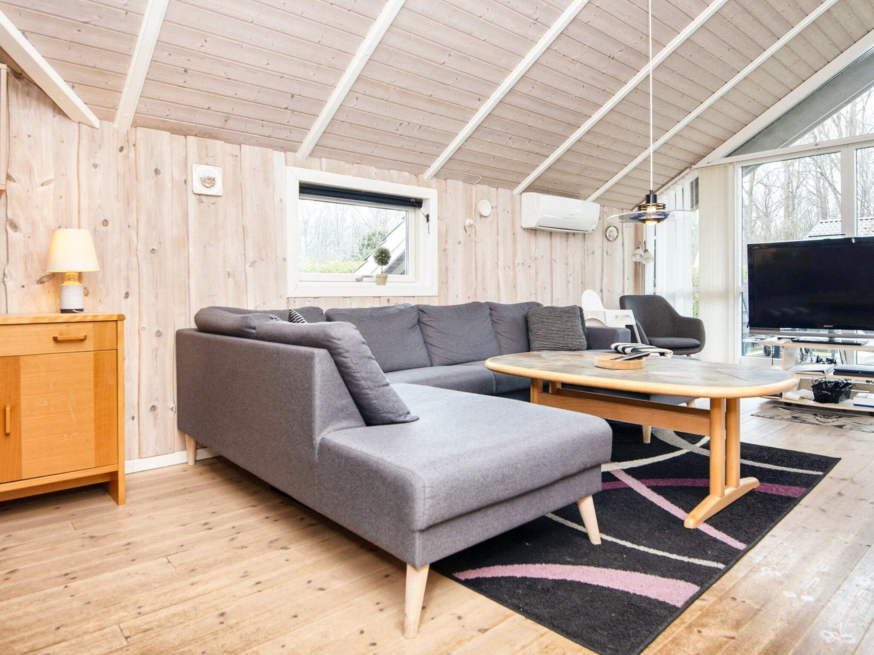 A modern living room with a grey sectional sofa, a wooden cabinet, a small table, and a flat-screen TV.