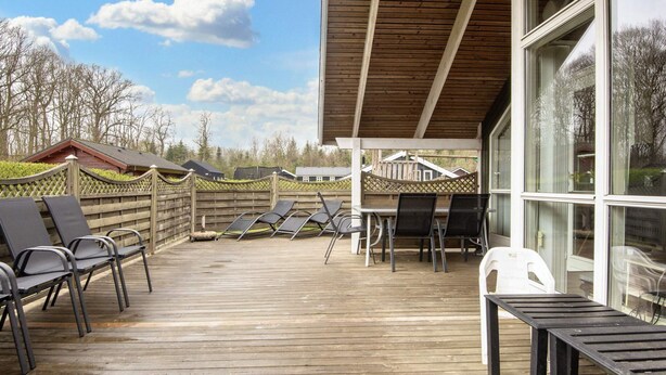 A covered outdoor area with wooden flooring, lounge chairs, and a table. - 5 Star Holiday Home in Juelsminde (Horsens)