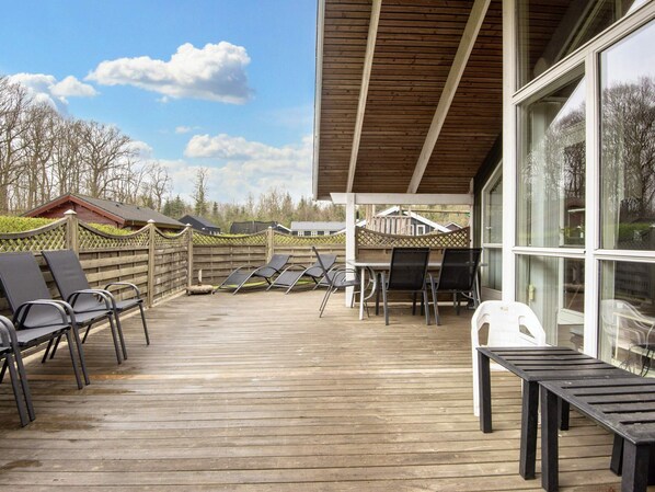 A covered outdoor area with wooden flooring, lounge chairs, and a table.