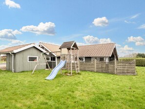A playground with a slide and a swing set, surrounded by a wooden fence and a grassy field. - 5 Star Holiday Home in Juelsminde (Horsens)