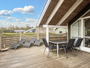 A covered outdoor area with a wooden deck, a table, and several chairs. - 5 Star Holiday Home in Juelsminde (Horsens)