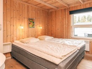 Una habitación con paneles de madera, una cama, dos luces fijadas a la pared y un ventanal.