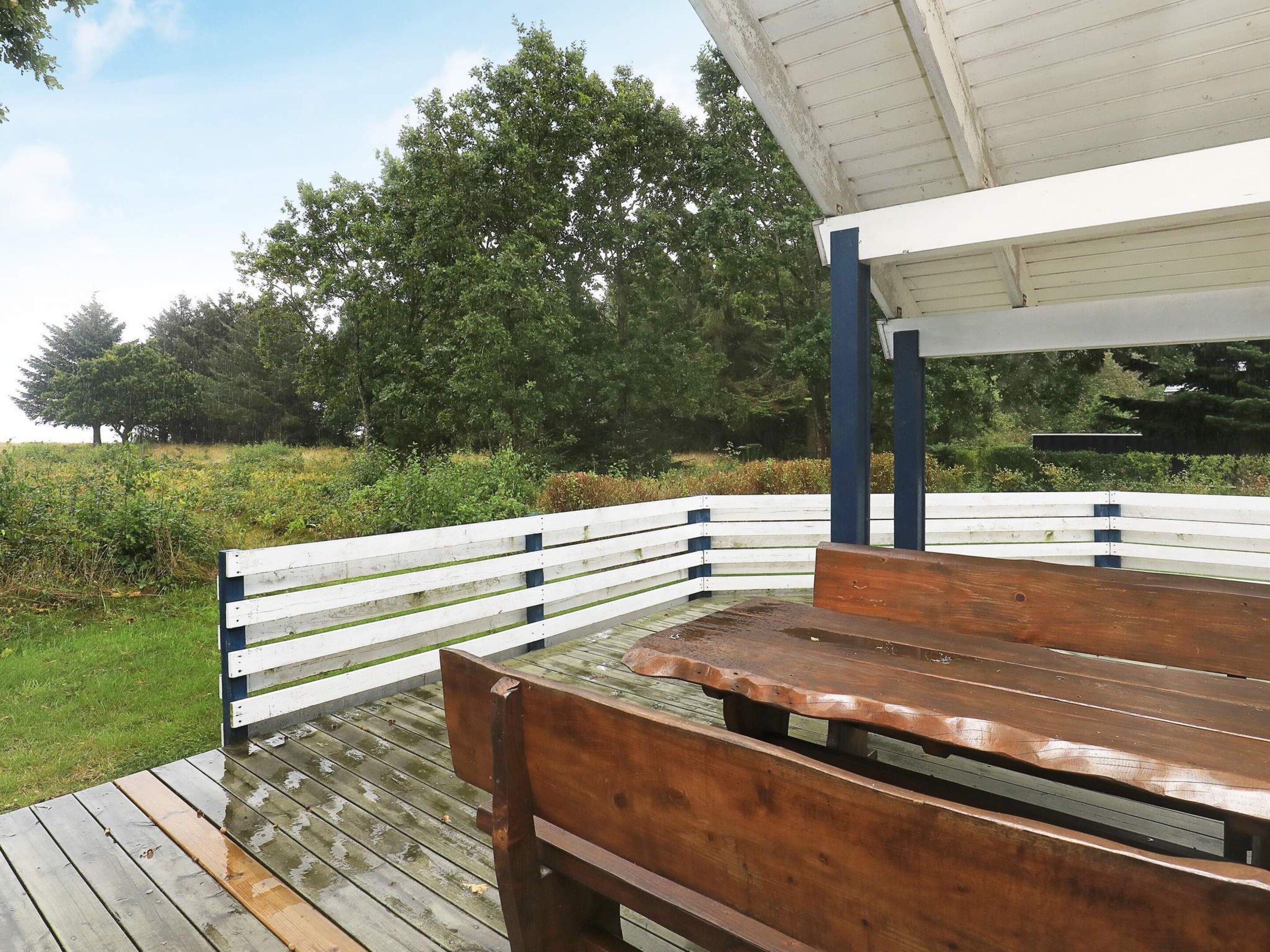 Une terrasse en bois avec un banc et un espace abrité, entourée de verdure.