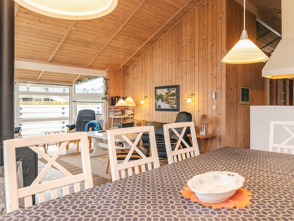 A cozy room with wooden walls, a dining table, chairs, and a view of the outside.
