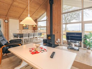A cozy living room with a fireplace, a dining area with a table and chairs, and a large window offering a view of the outdoors.