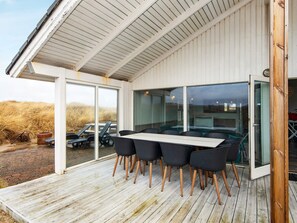 A covered outdoor seating area with a table and chairs, large windows, and a view of the surrounding landscape. - 4 Star Holiday Home in Henne (Henne)