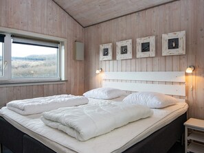 A bedroom with a wooden headboard, a large bed with white bedding, a window with a view, and wall-mounted picture frames. - 4 Star Holiday Home in Henne (Henne)