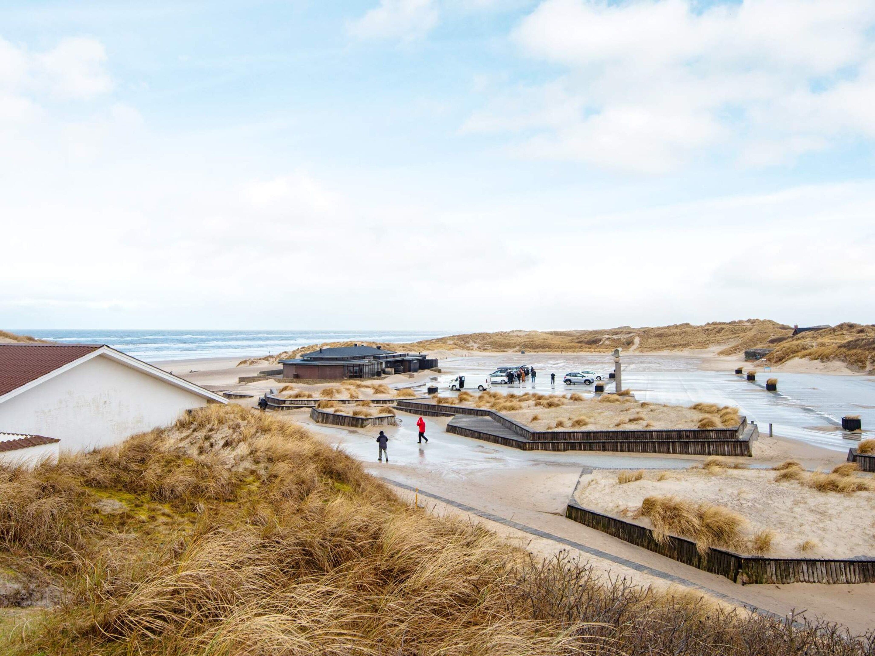Een kustgebied met gebouwen, een zandstrand en duinen.