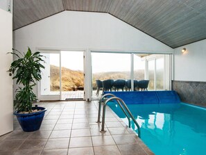 An indoor swimming pool with a view of the outdoors, a potted plant, and a seating area with chairs. - 4 Star Holiday Home in Henne (Henne)
