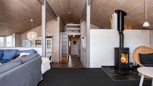 A modern interior with a sofa, a dining table, a fireplace, and a staircase leading to an upper level. - 4 Star Holiday Home in Henne (Henne)