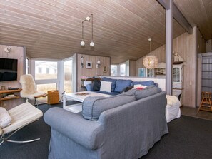 A modern living room with a grey sofa, a white chair, and a television mounted on the wall. - 4 Star Holiday Home in Henne (Henne)