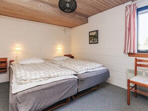 Una habitación con dos camas, una silla, un cuadro en la pared y un ventanal con cortinas.