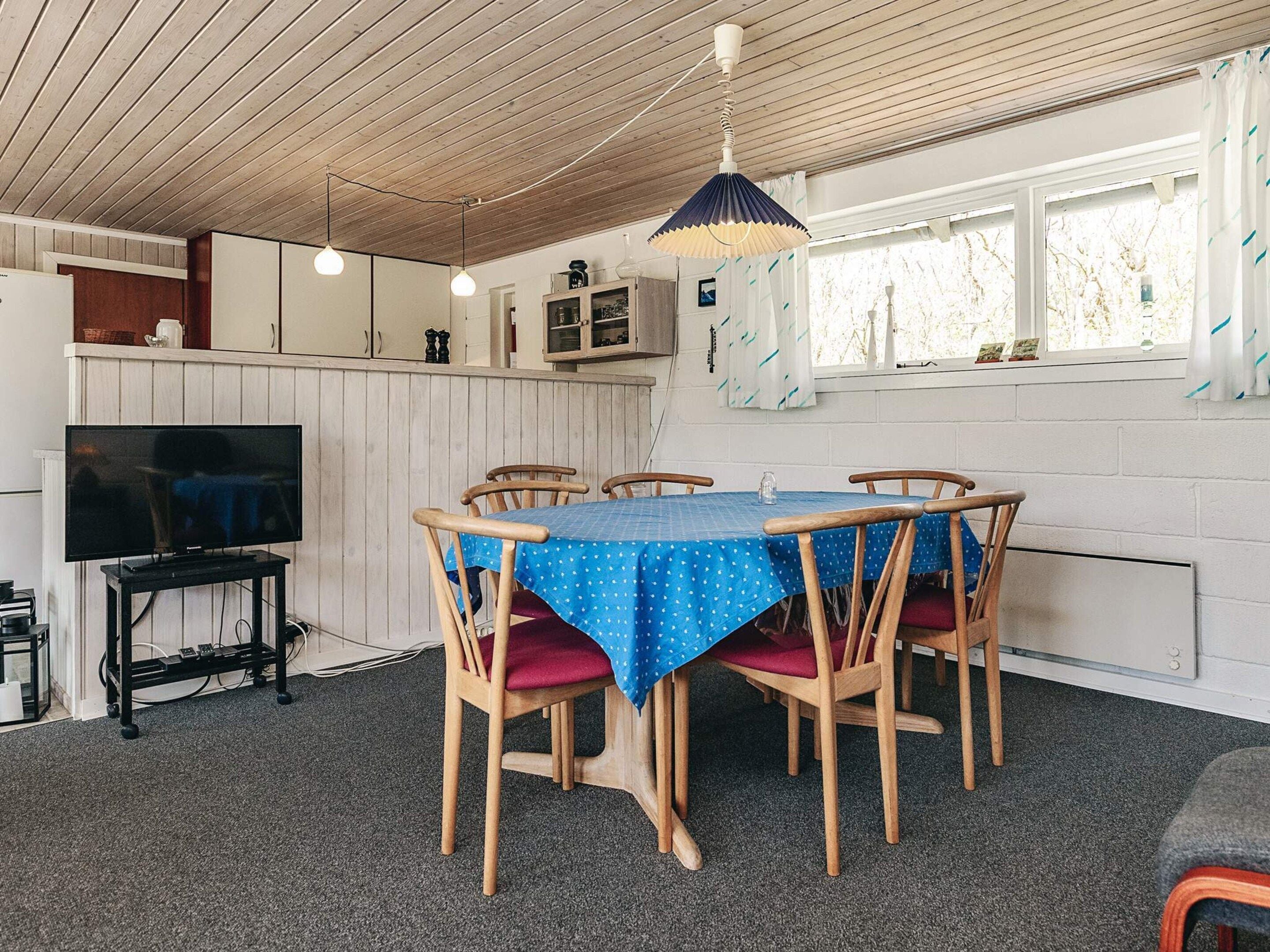 En matplats med ett bord för fyra personer, trästolar, en tv på ett stativ och ett tak med synliga träbjälkar.