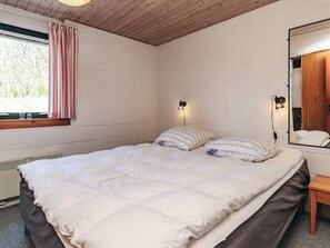 A bedroom with a bed, a window with curtains, a wall-mounted lamp, and a mirror.