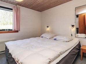 A bedroom with a bed, a window with curtains, a wall-mounted lamp, and a mirror.