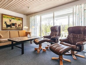 A room with a sofa, two leather recliners, a coffee table, and a painting of deer.