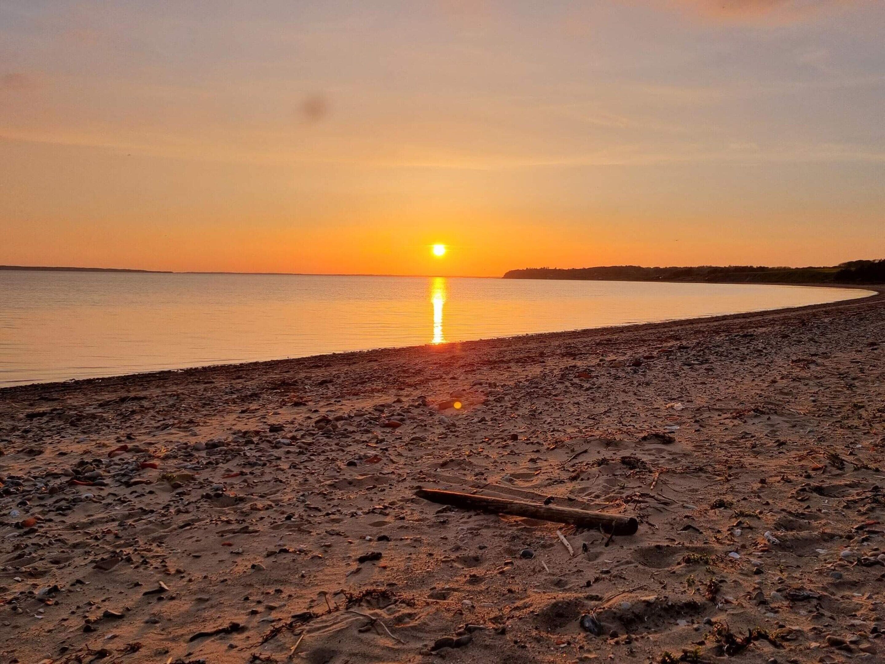 A beach with a sunset, calm water, and a distant shoreline.