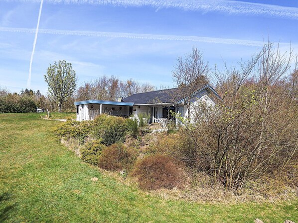A house with a sloped roof, a porch with chairs, and a lawn.