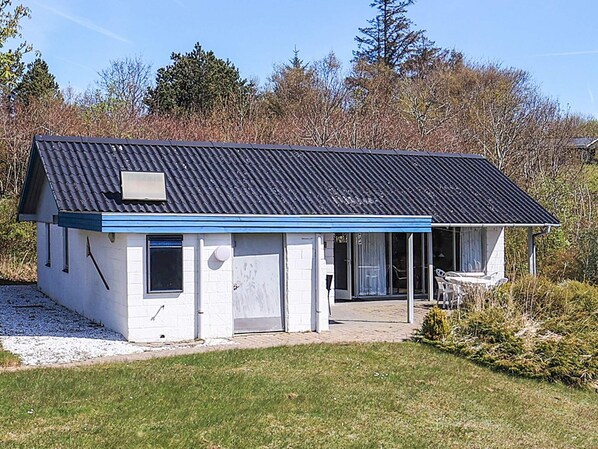 Ett envåningshus med ett mörkt tak, en inglasad veranda och en liten trädgård framför huset.