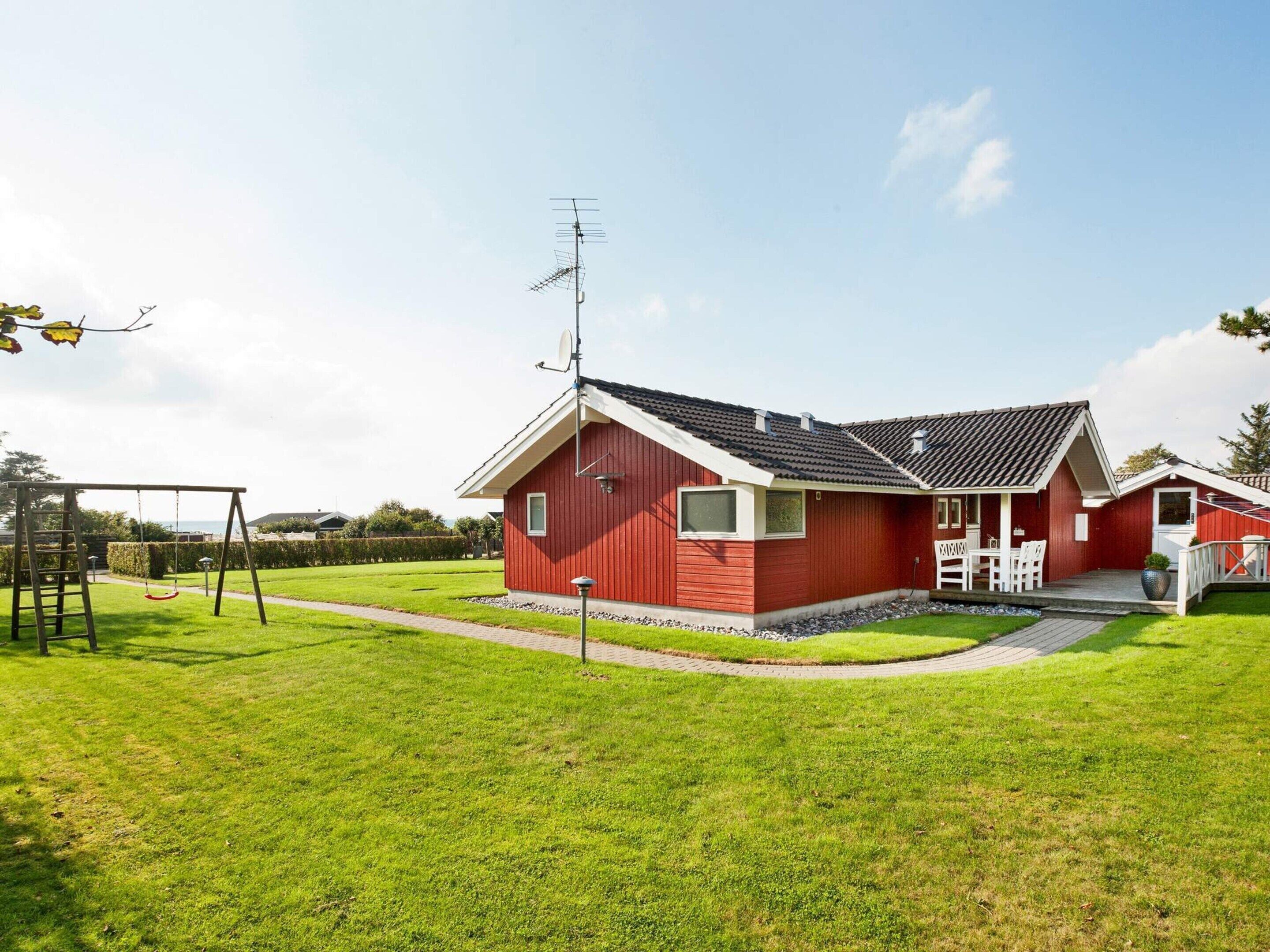 Ein rotes Haus mit Satellitenschüssel, Schaukel und gepflasterter Auffahrt.