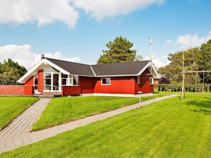 A red building with a sloped roof, a paved pathway, and a grassy area.