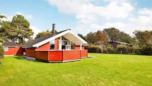Una casa roja con techo blanco, patio cercado y una escalera apoyada en un árbol.