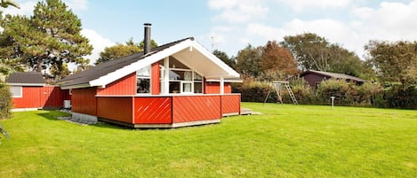A red house with a white roof, a fenced yard, and a ladder leaning against a tree.