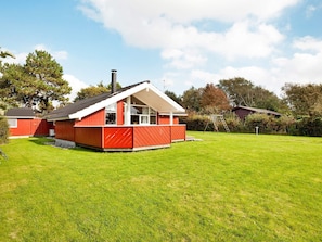 A red house with a white roof, a fenced yard, and a ladder leaning against a tree.