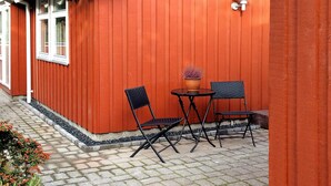 Un espace extérieur aménagé avec deux chaises et une table, un pot de fleurs et un luminaire fixé au mur.