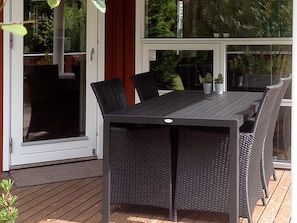 A covered outdoor dining area with a table and chairs, a sliding glass door, and potted plants.