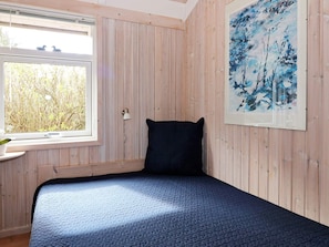 A room with a bed, a window, a wall-mounted lamp, and a painting.