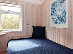 A room with a bed, a window with a view of trees, a wall-mounted lamp, and a painting.