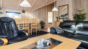 A modern living room with a wooden ceiling, a black leather sofa, a dining table with chairs, and a coffee table with a tray.