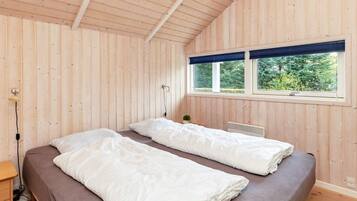 A room with two beds, a window with a view of greenery, and a lamp.