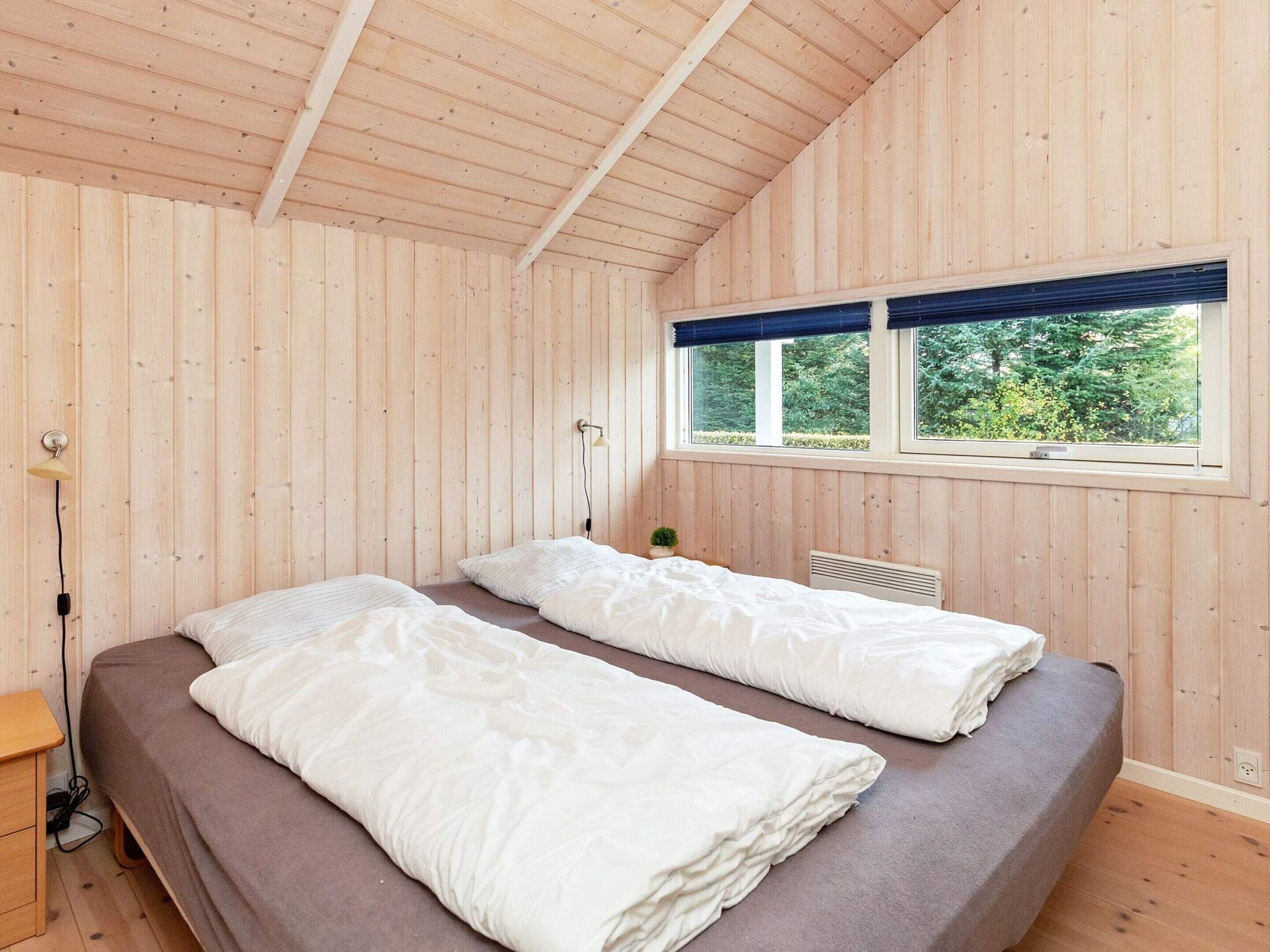 A room with two beds, a window with a view of greenery, and a lamp.