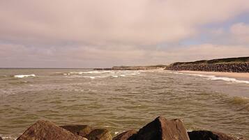 A coastal beach scene with waves, rocks, and a distant shoreline.