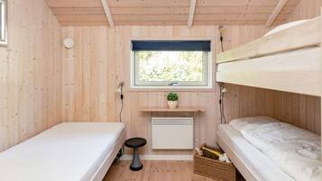 A small, wooden room with bunk beds, a window, a radiator, and a small stool.