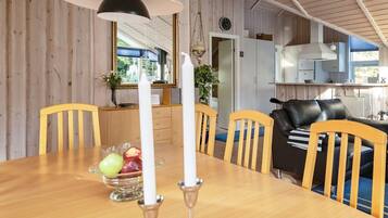 A wooden interior with a dining table, chairs, a black leather sofa, and a kitchen area with a window.