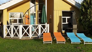 En gul bygning med hvidt hegn, grill og tre liggestole.